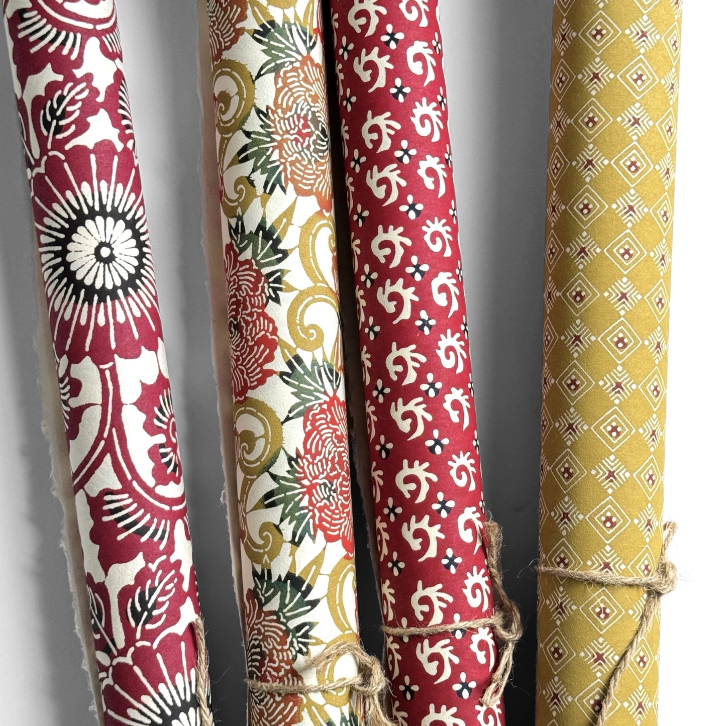 Japanese Katazome-shi stencil-dyed paper with repeat pattern on stylised peonies in autumnal colours. Pictured rolled with other paper designs.