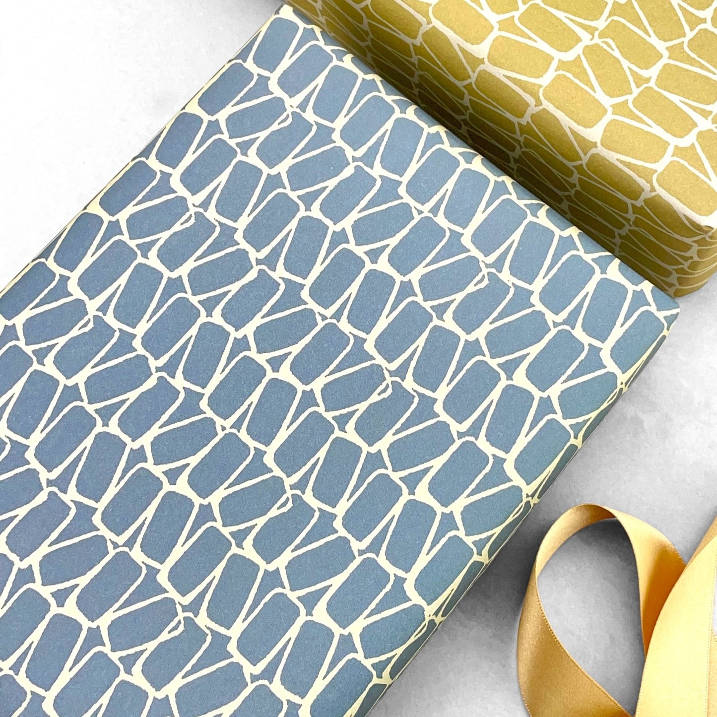 wrapping paper by Anne Davison Studio. Creamy domino outlined shapes on a dusky blue background.  shown wrapped as a present