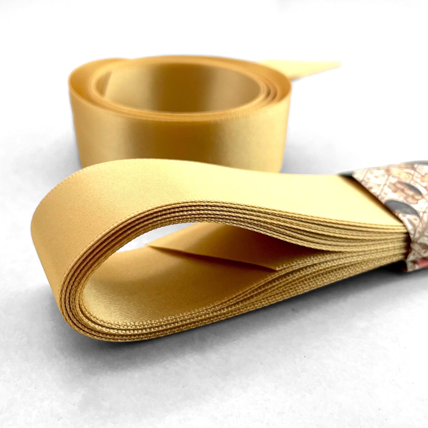 Satin ribbon 25mm wide and 5 metres long, presented with a patterned paper band. colour - honey gold