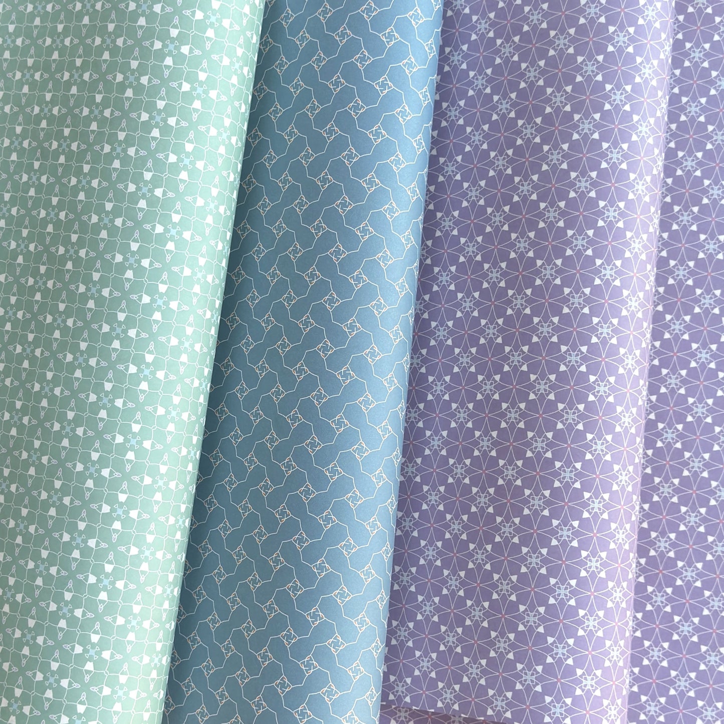 Three wrapping papers with geometric patterns in green, blue, and purple.