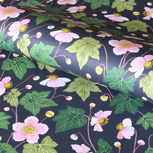a sheet of wrapping paper with a dark indigo background and pink japanese anemone flowers and green foliage