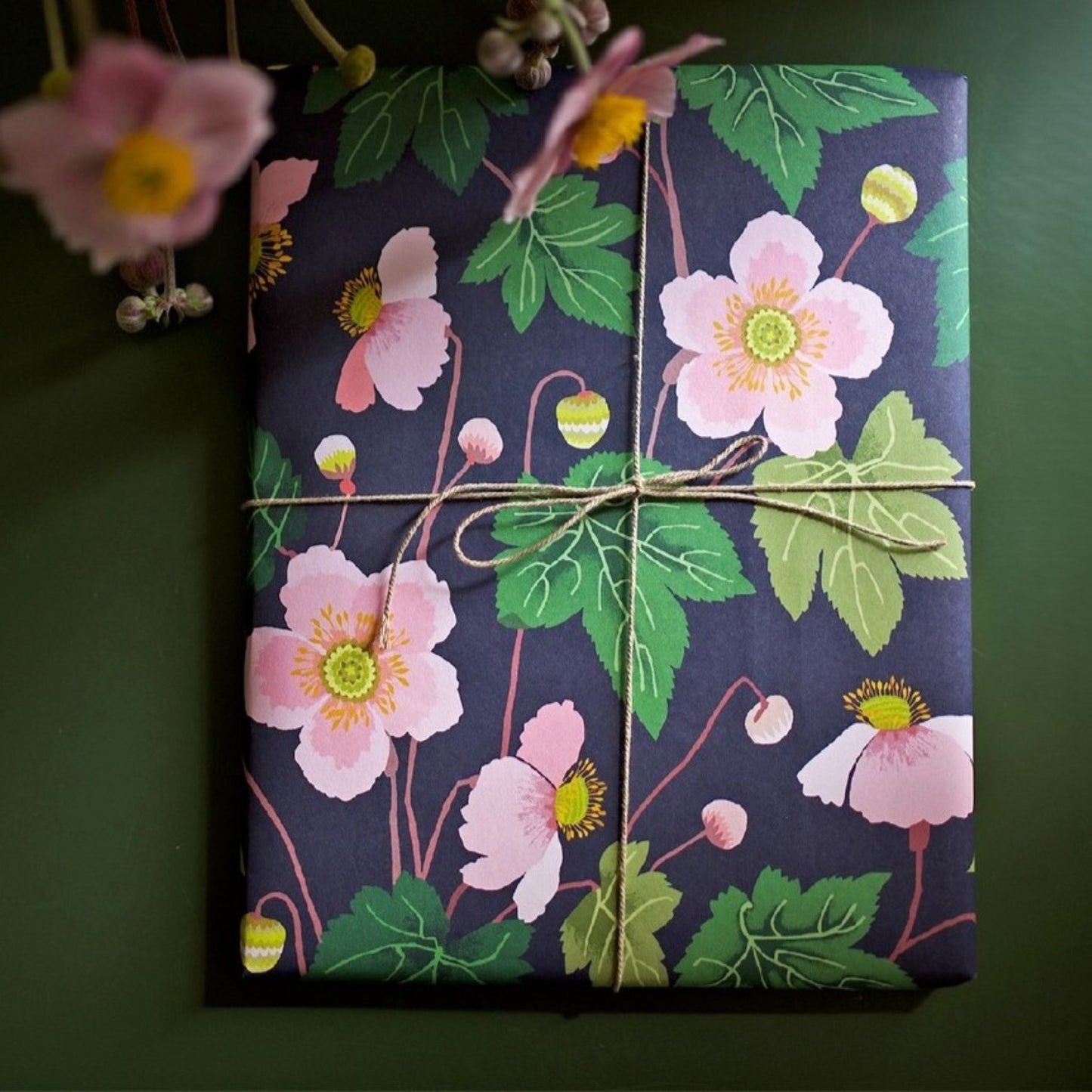 a sheet of wrapping paper with a dark indigo background and pink japanese anemone flowers and green foliage