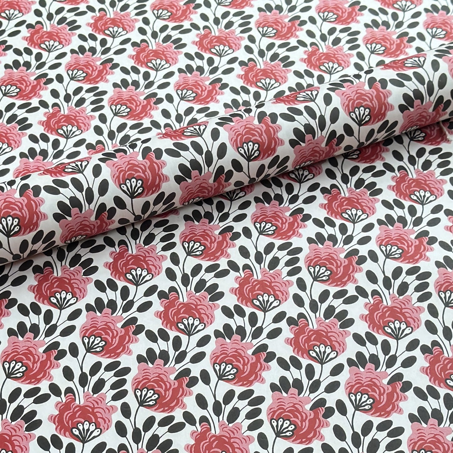 wrapping paper with a repeat design of pink flowers, black seedheads on white