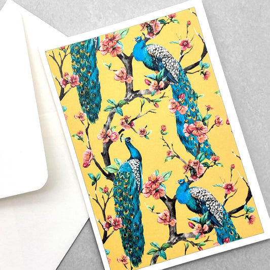 greetings card of four peacocks in a tree in blossom with yellow backdrop by Com Bossa Studio