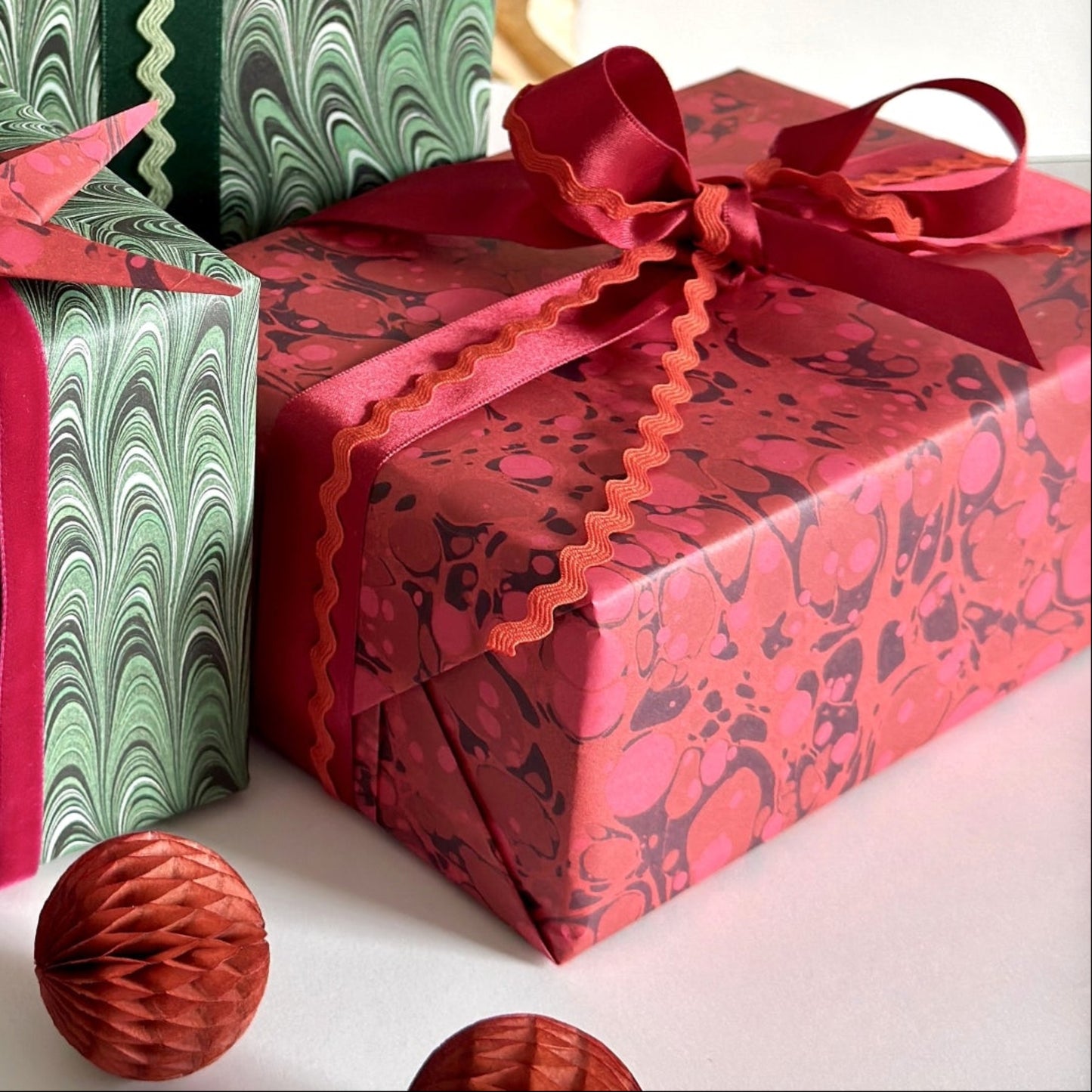 a pile of presents wrapped in printed marble papers in green swirls and deep red spotted wrapping paper