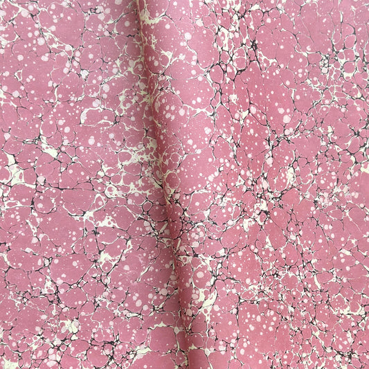 a sheet of wrapping paper with a pink marbled pattern with white and black veined design