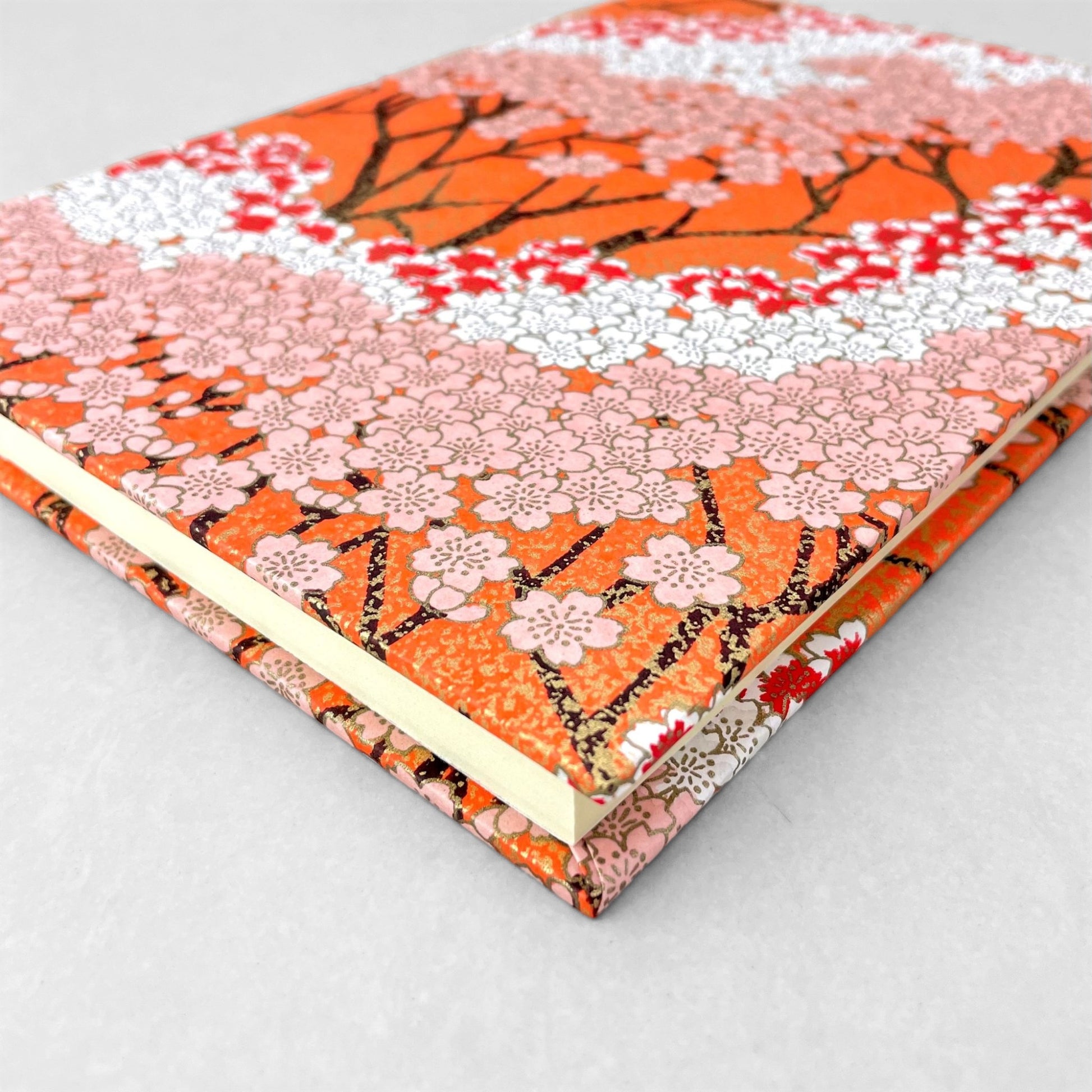 hardback A5 plain notebook with cover made of japanese silkscreen chiyogami paper. Pink and white cherry blossom design on peach background by Esmie
