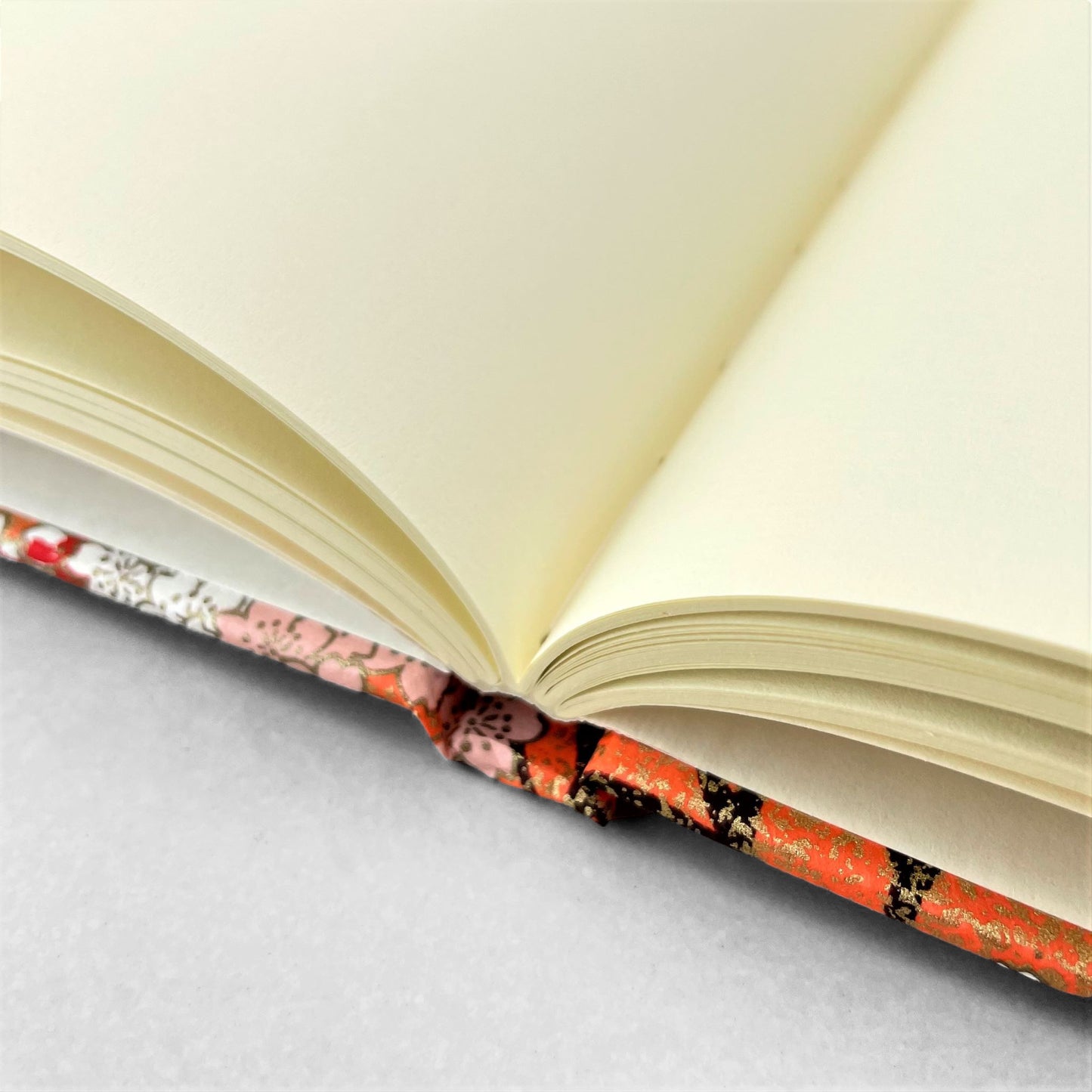 hardback A5 plain notebook with cover made of japanese silkscreen chiyogami paper. Pink and white cherry blossom design on peach background by Esmie