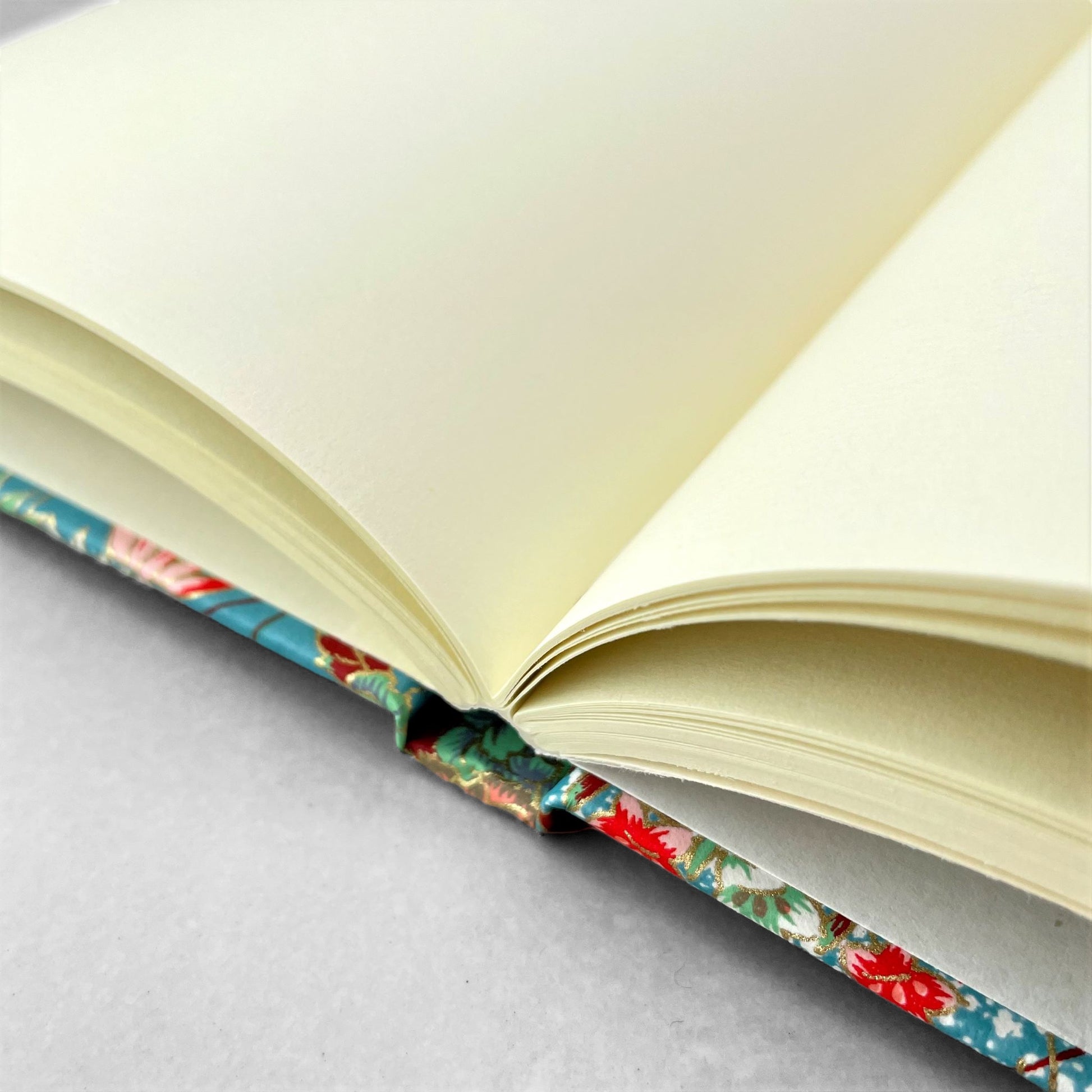 hardback A5 plain notebook with cover made of japanese silkscreen chiyogami paper. Multicolour floral bouquet pattern on teal background by Esmie