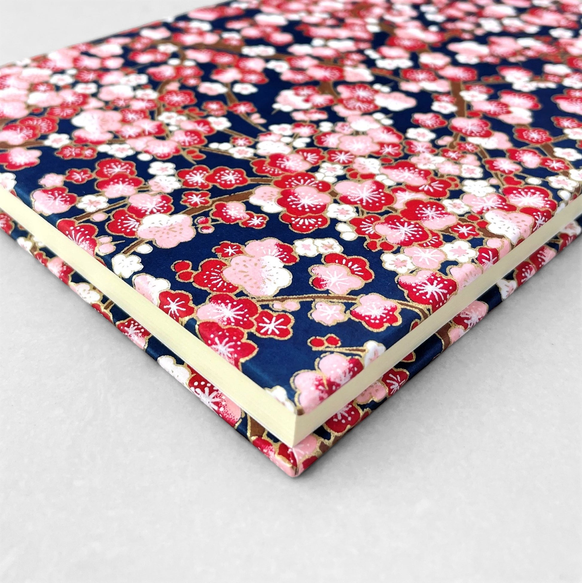 hardback A5 plain notebook with cover made of japanese silkscreen chiyogami paper. Pink and burgundy cherry blossom design on dark blue backdrop by Esmie