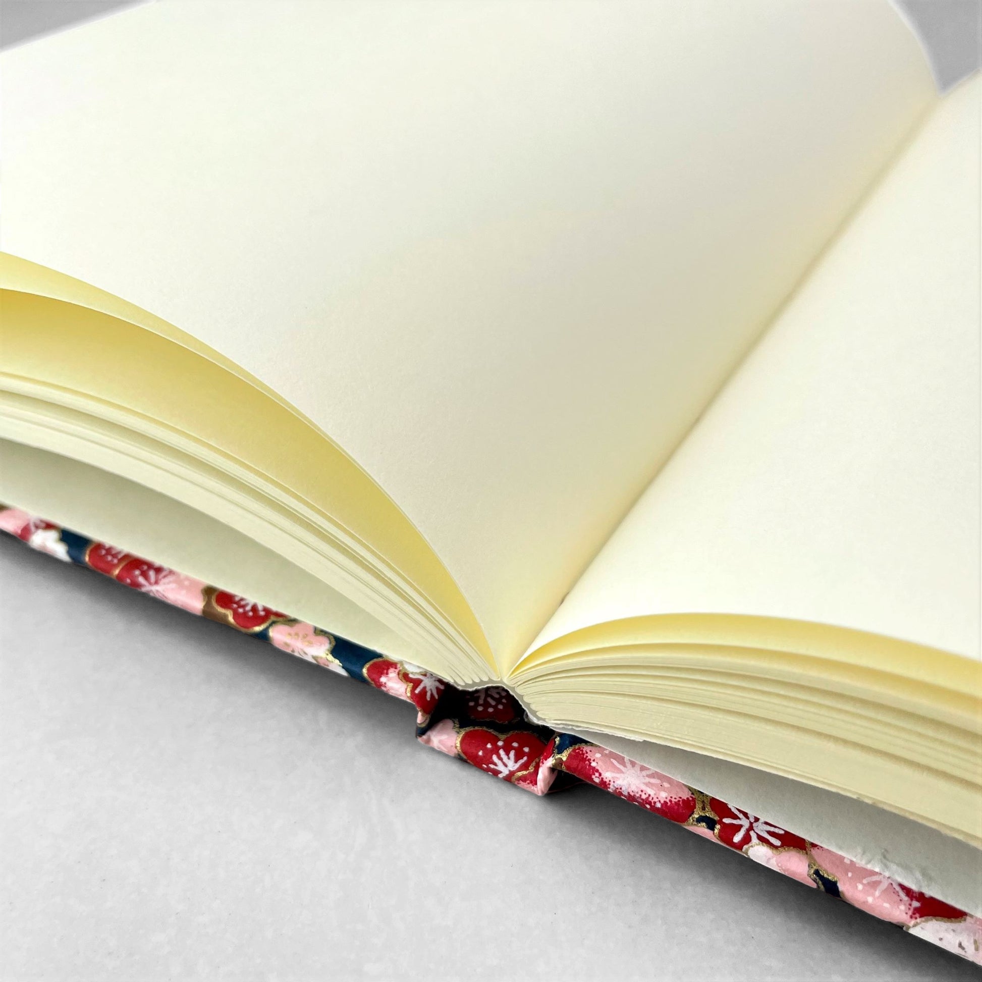hardback A5 plain notebook with cover made of japanese silkscreen chiyogami paper. Pink and burgundy cherry blossom design on dark blue backdrop by Esmie