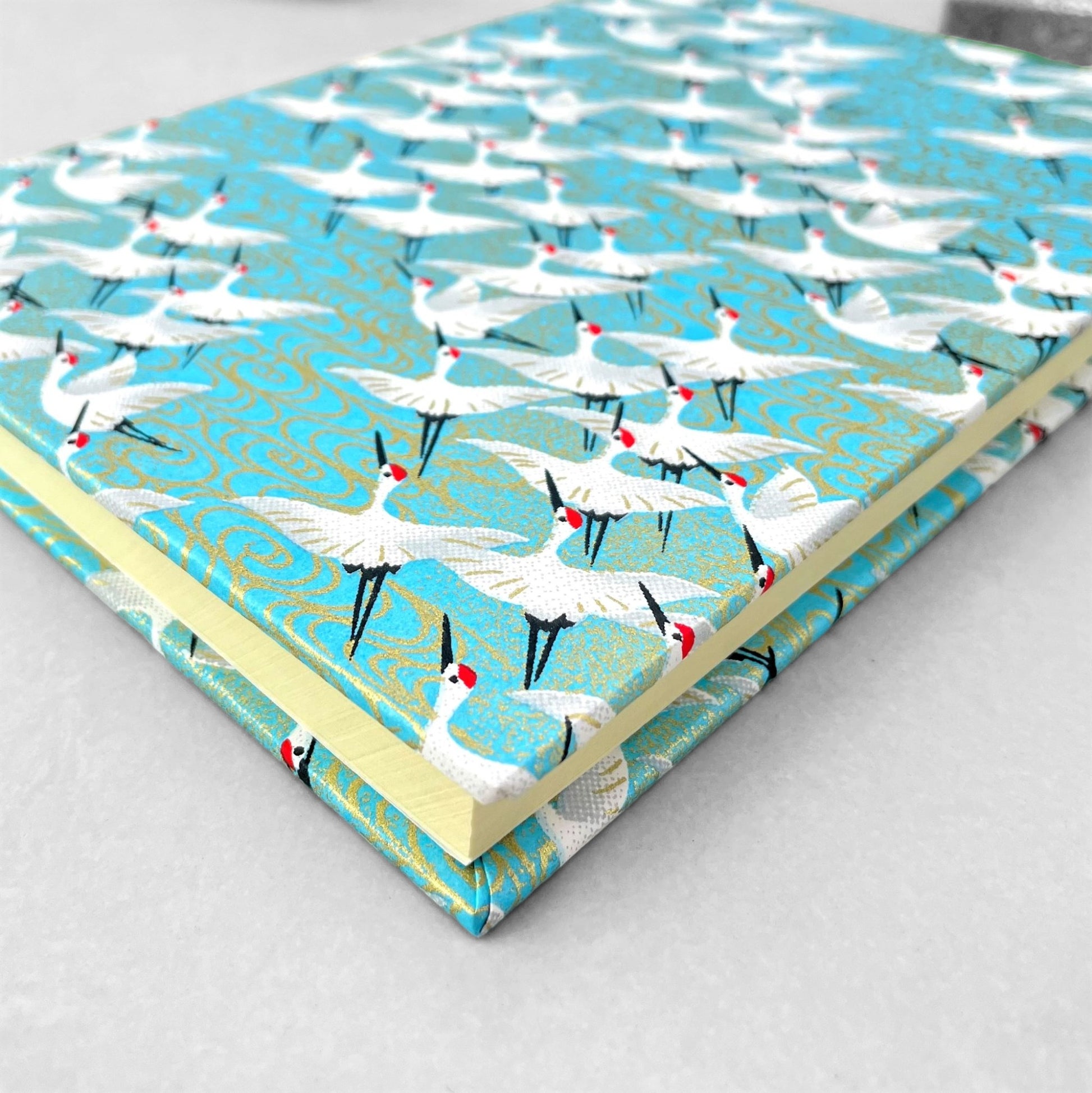 hardback A5 plain notebook with cover made of japanese silkscreen chiyogami paper. White cranes in flight on a pale blue background by Esmie