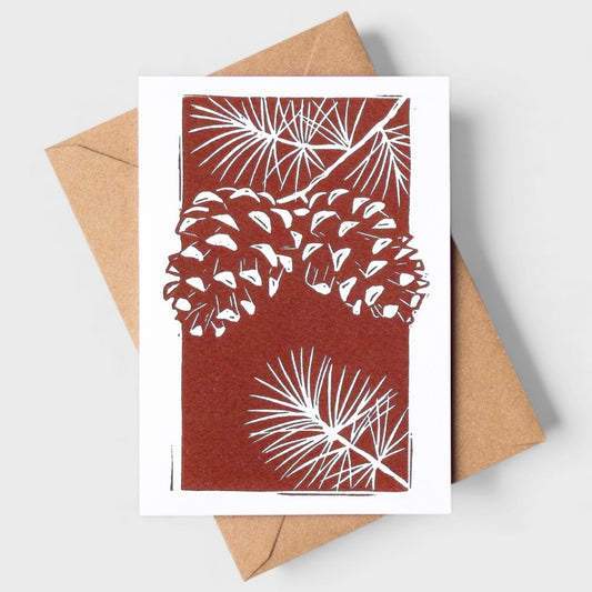 Greeting card with pine cone and branch design on a brown background, accompanied by a brown envelope.