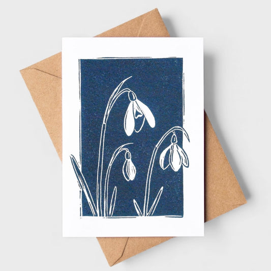 Greeting card with snowdrop design on a blue background, accompanied by a brown envelope.