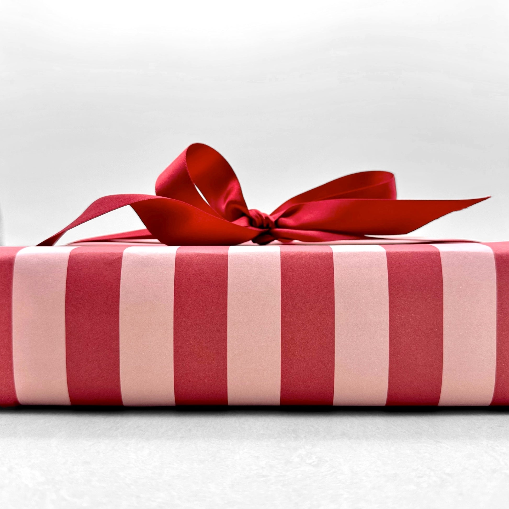 wide classic stripe wrapping paper in red and pink by Heather Evelyn, pictured wrapped with a red bow