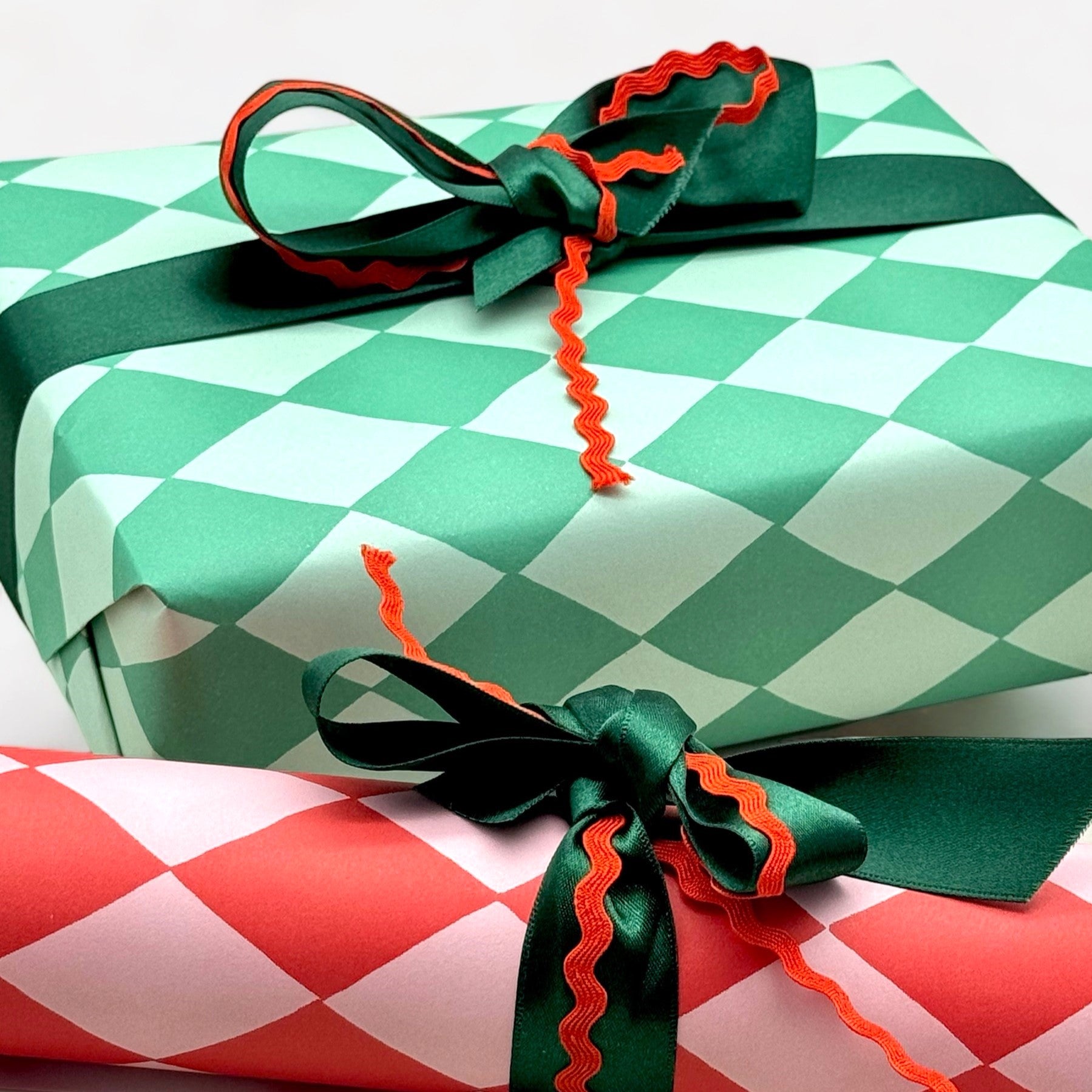 a sheet of wrapping paper with a two tone green large diamond pattern. By Heather Evelyn and shown wrapped as a gift with green satin ribbon and red rik rac bow