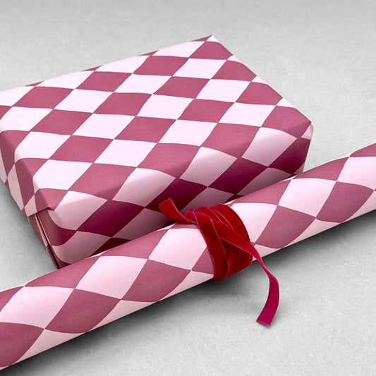 wrapping paper with large diamond design in mauve and pink. Pictured wrapped as a present with a roll of the patterned paper alongside. By Heather Evelyn