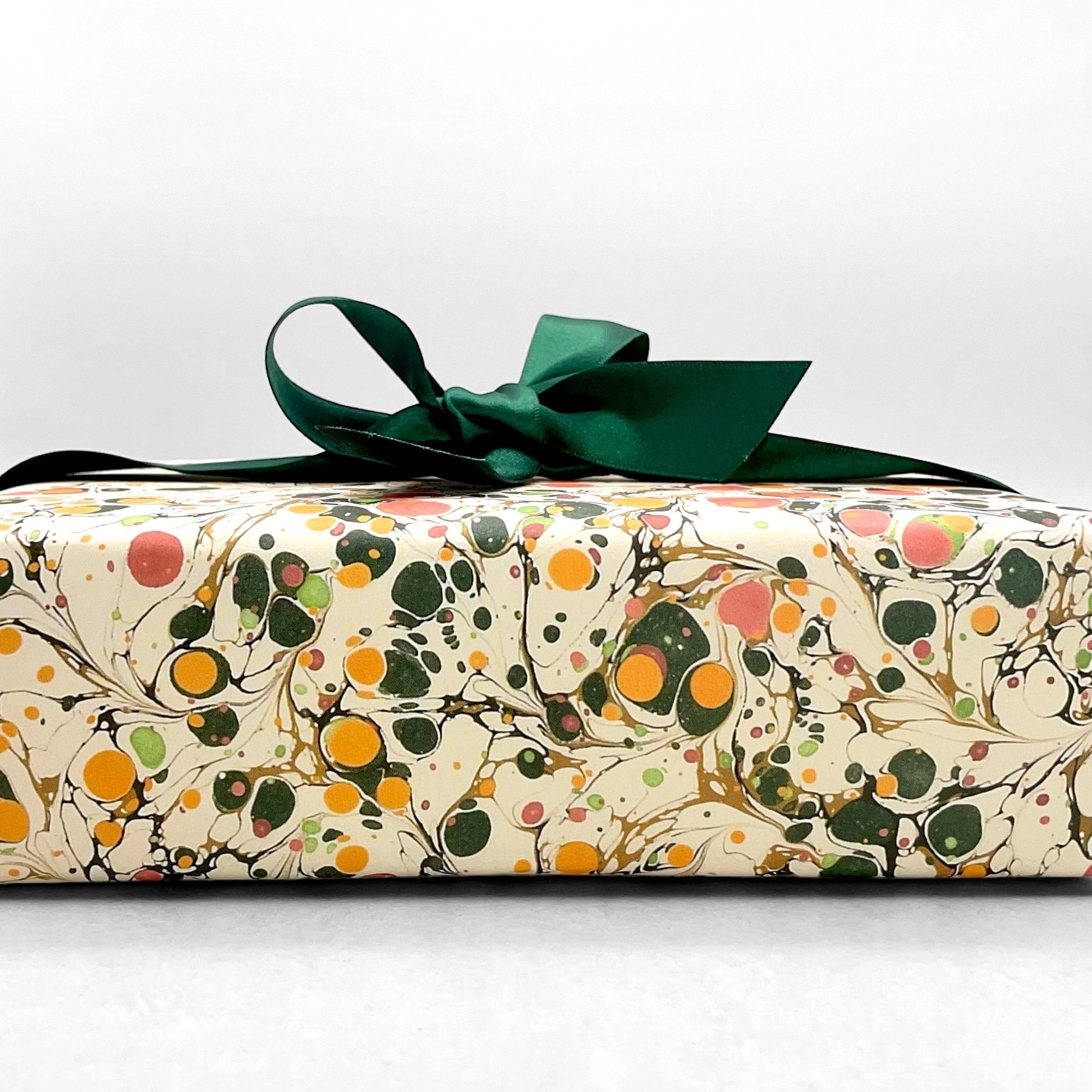 Printed marbled wrapping paper by Jemma Lewis Marbling. Marbled paper in bright yellow, pink and green on white backdrop. Pictured wrapped with a bow