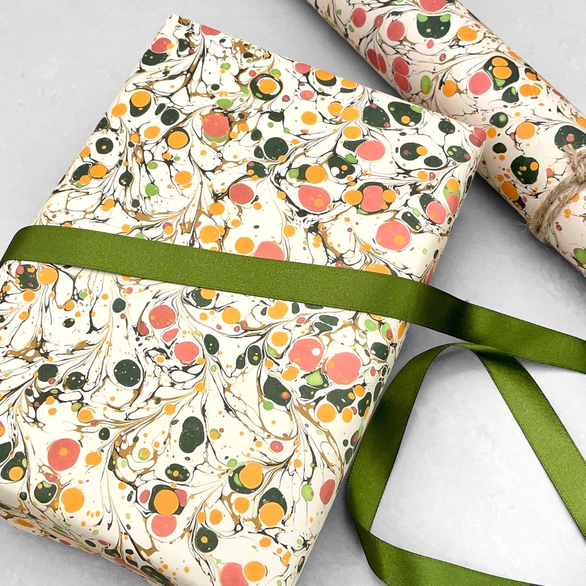 Printed marbled wrapping paper by Jemma Lewis Marbling. Marbled paper in bright yellow, pink and green on white backdrop. Pictured with green ribbon