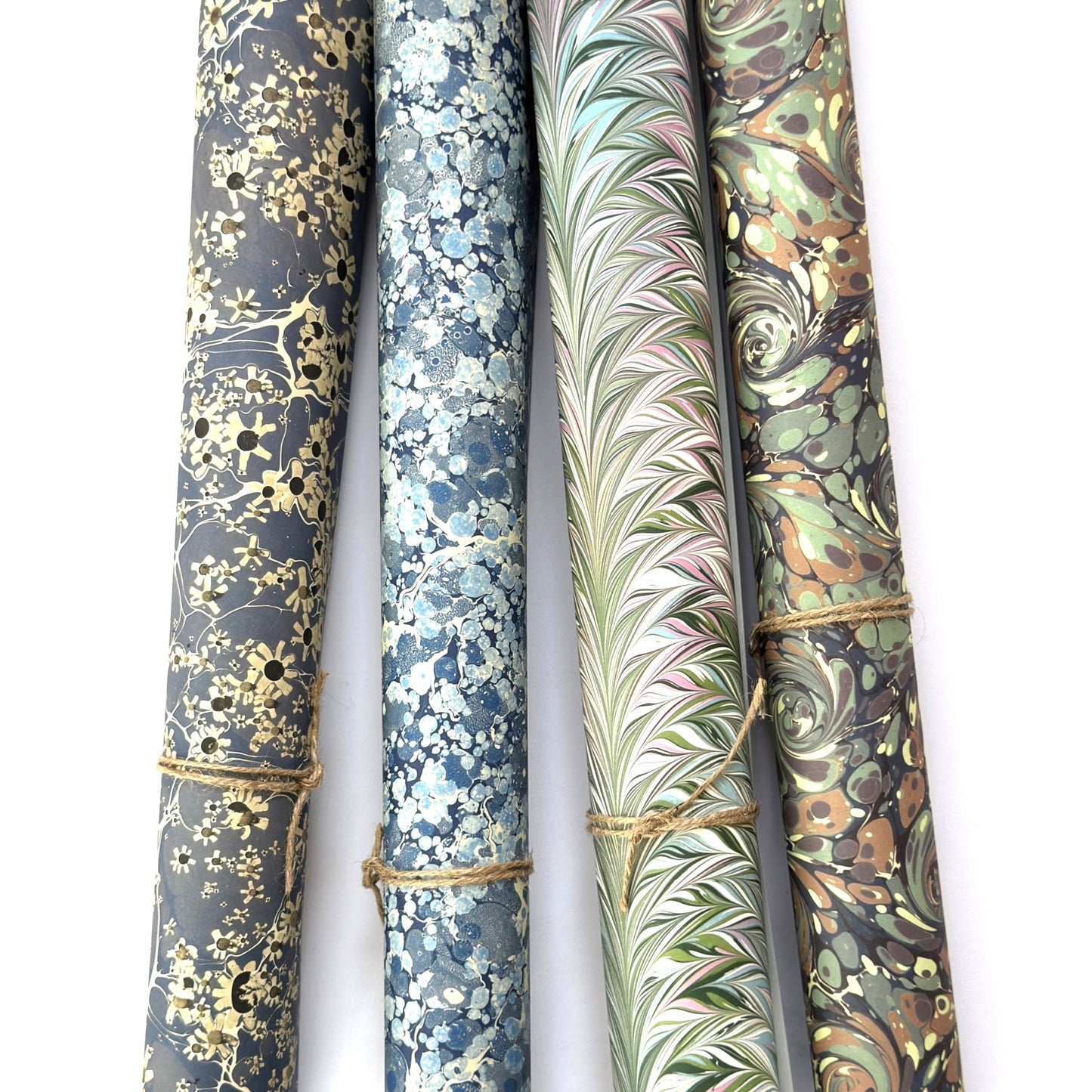 printed marble design wrapping paper by Jemma Lewis. Daisy flower design in white and black on blue backdrop. Pictured rolled with other designs in the collection