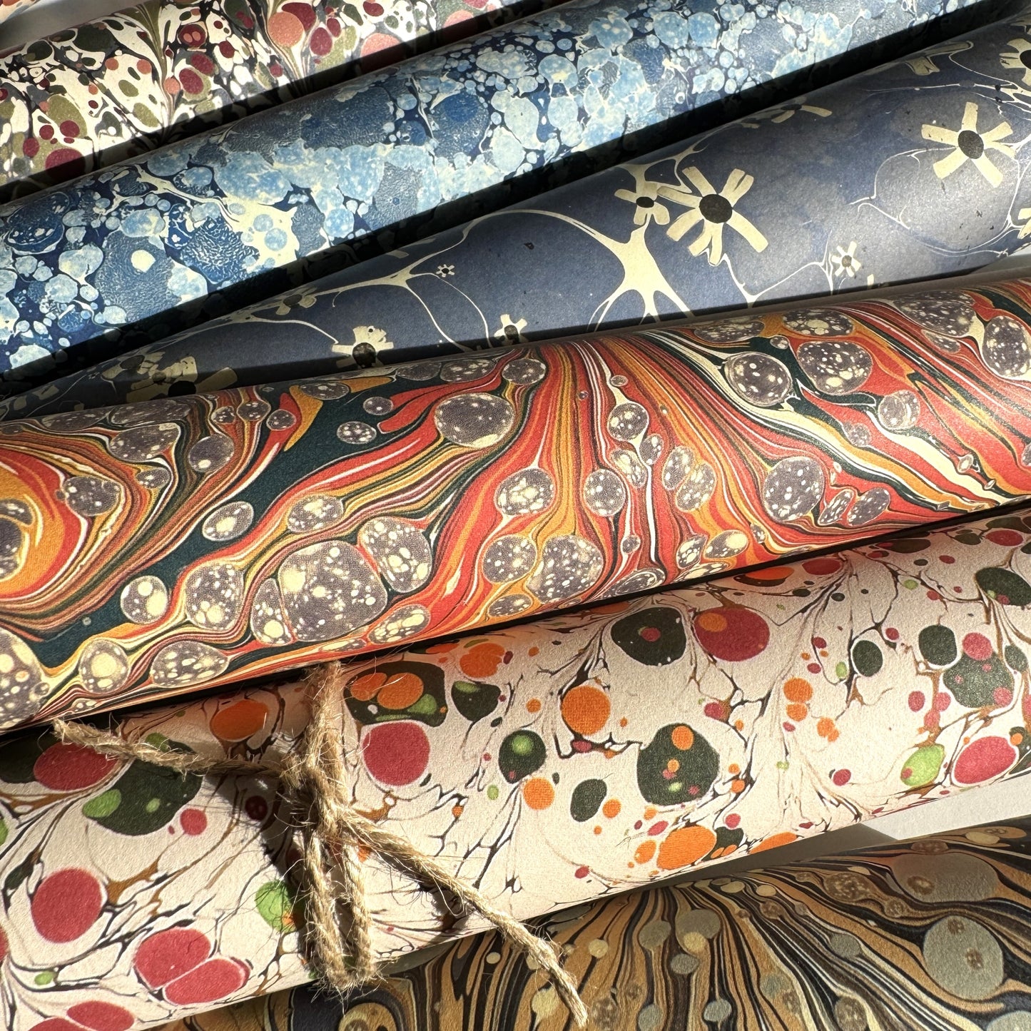 printed marbled design wrapping paper by jemma lewis. marbled stone design in red, yellow and grey. Pictured with other marble design papers, rolled