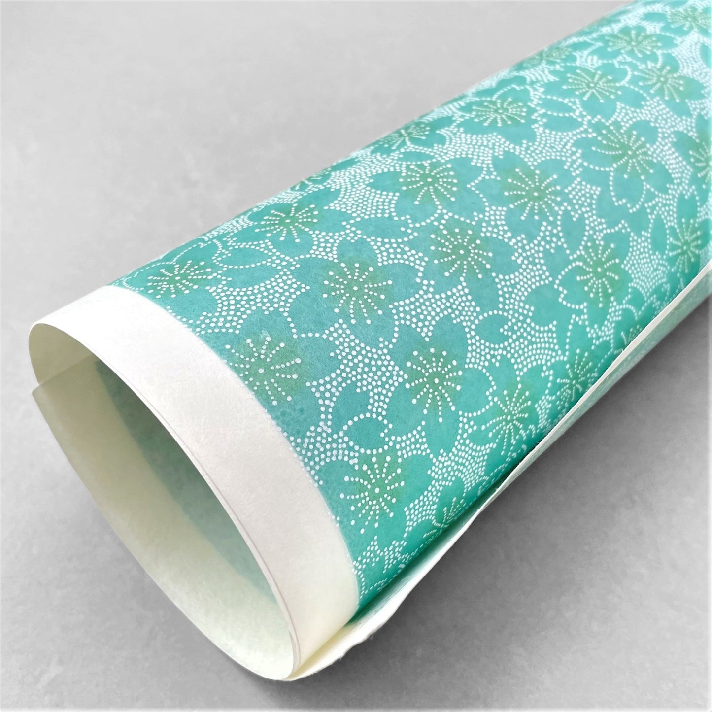 japanese silk-screen paper, chiyogami, with a cherry blossom flower repeat pattern in turquoise and white