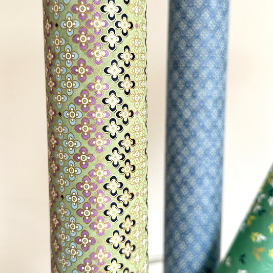 Japanese silkscreen chiyogami paper with a repeat pattern of stripes of a small floral motif in black, lilac and blue on a moss green backdrop, close up