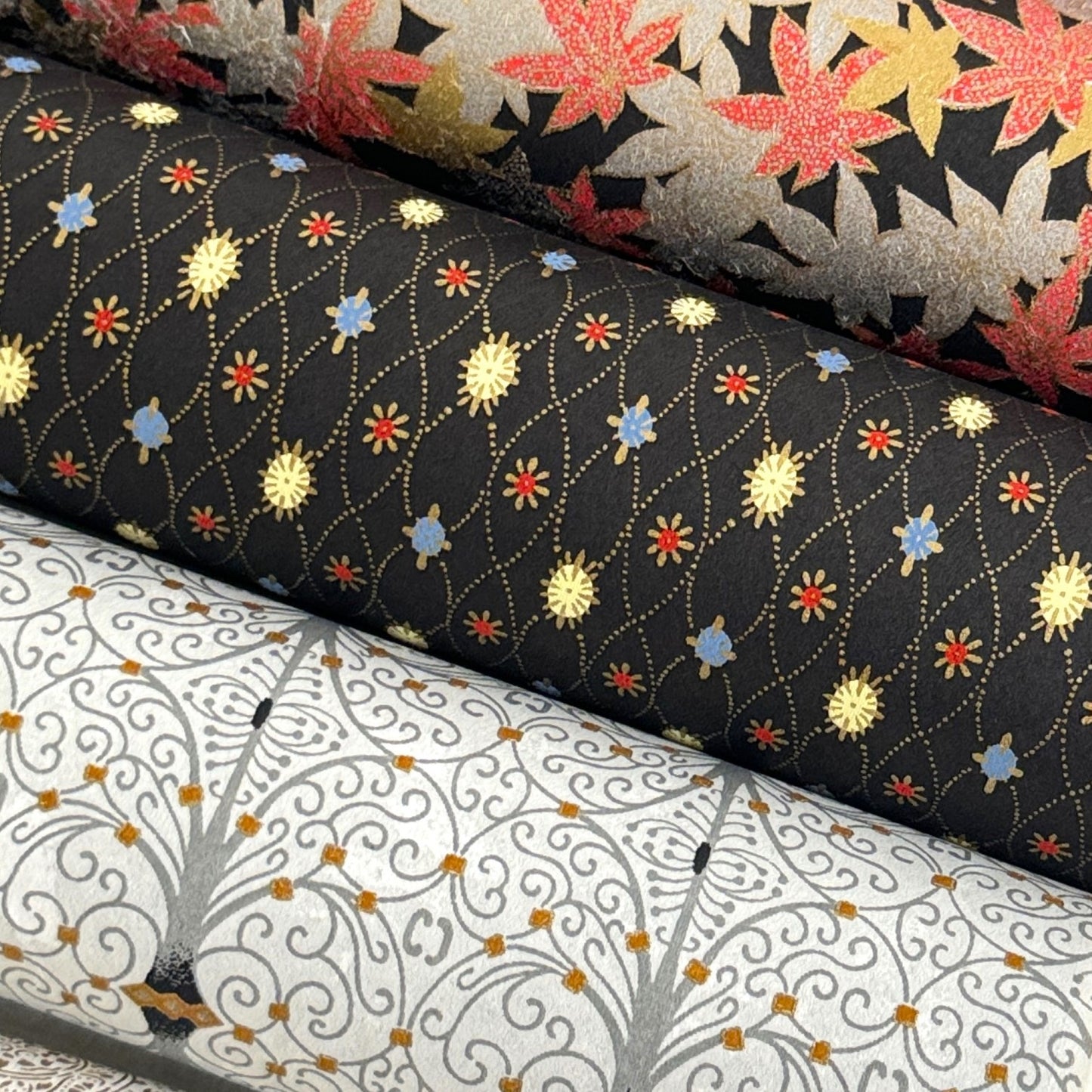 Japanese silkscreen chiyogami paper with a pattern of small repeat motifs in red, blue, lemon and gold on a black background, close up