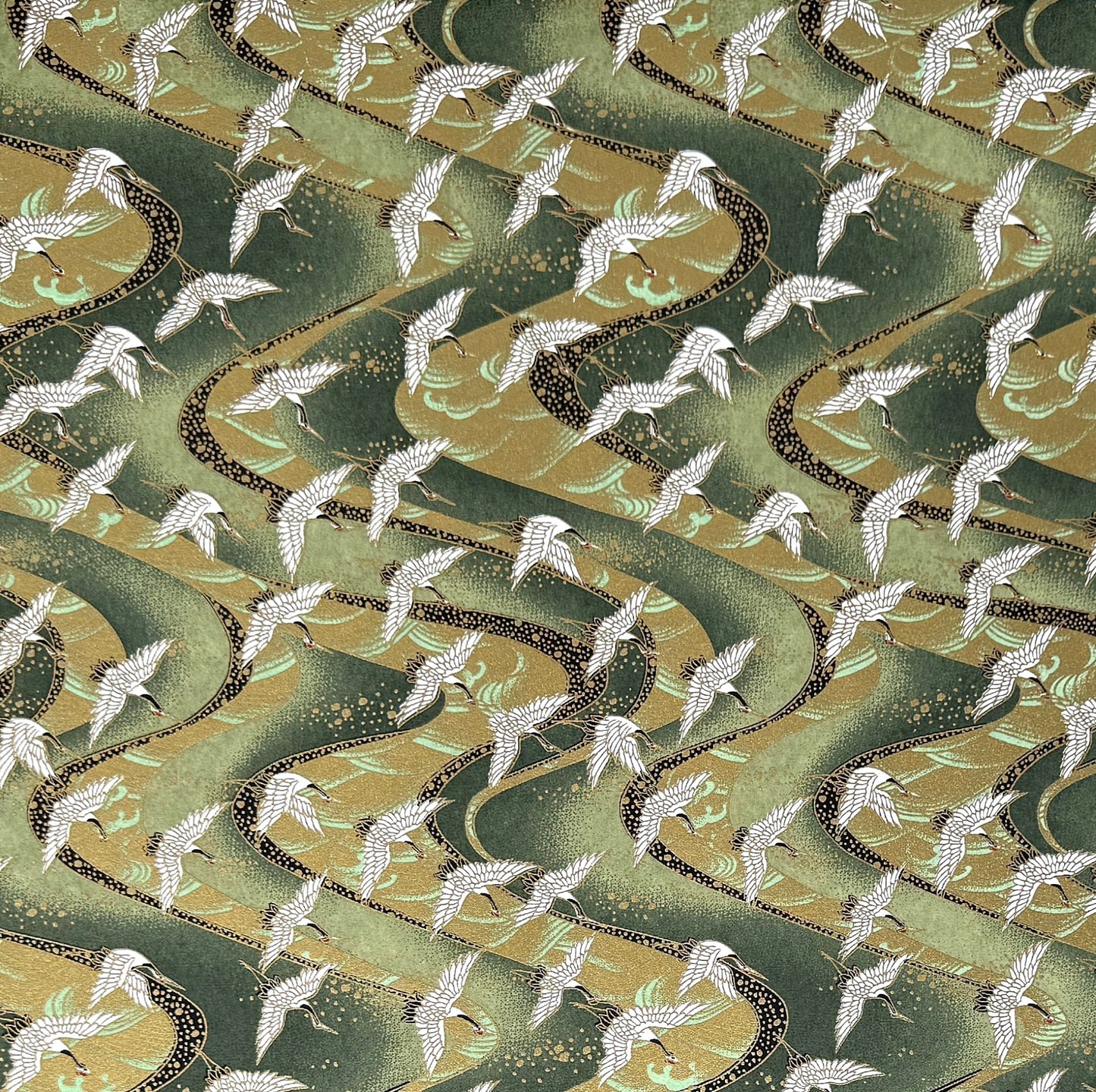 a sheet of Japanese chiyogami paper with white cranes flying on a dark green and gold swirl background