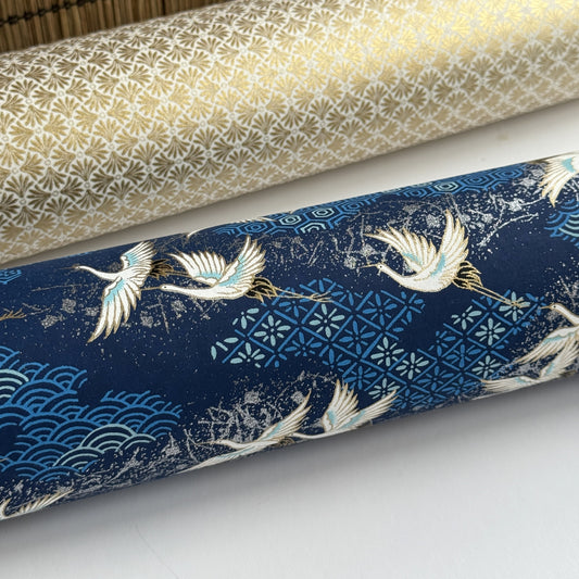 a sheet of Japanese chiyogami yuzen paper with a traditional pattern of white cranes flying with a deep blue background of patterned clouds. Close up and pictured rolled