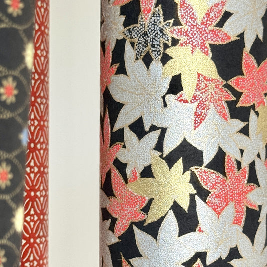 Japanese silkscreen chiyogami paper with an abundance of falling maple leaves in red, gold and silver on black backdrop, close up