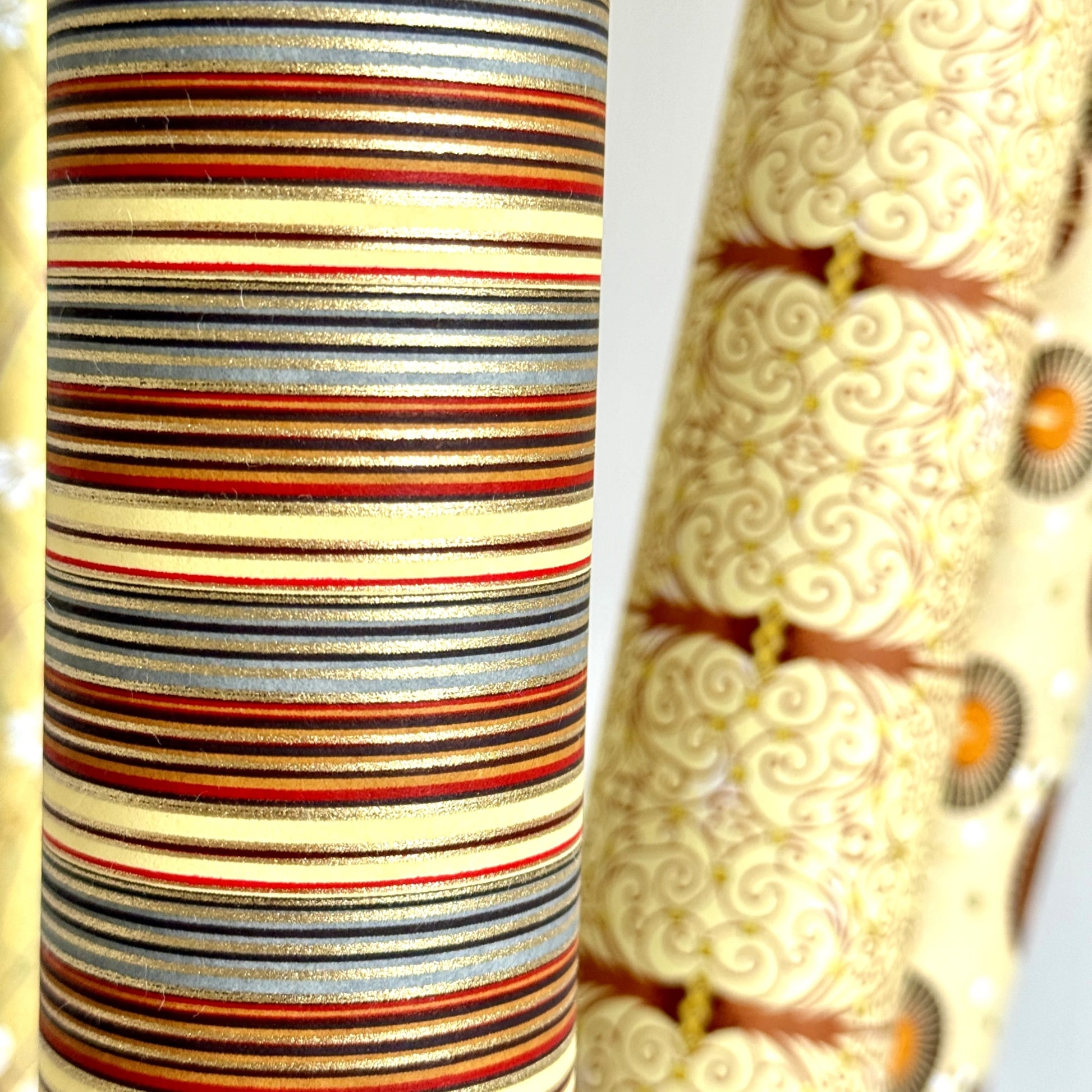 Japanese silkscreen chiyogami paper with a classic narrow stripe pattern in earthy tones of brown, grey, cream, black and gold. Close up