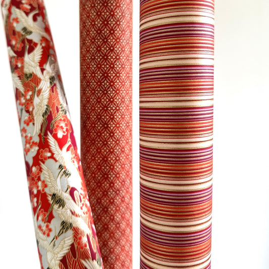 Japanese silkscreen chiyogami paper with a classic narrow stripe pattern in berry tones of red, pink, purple and gold. Close up