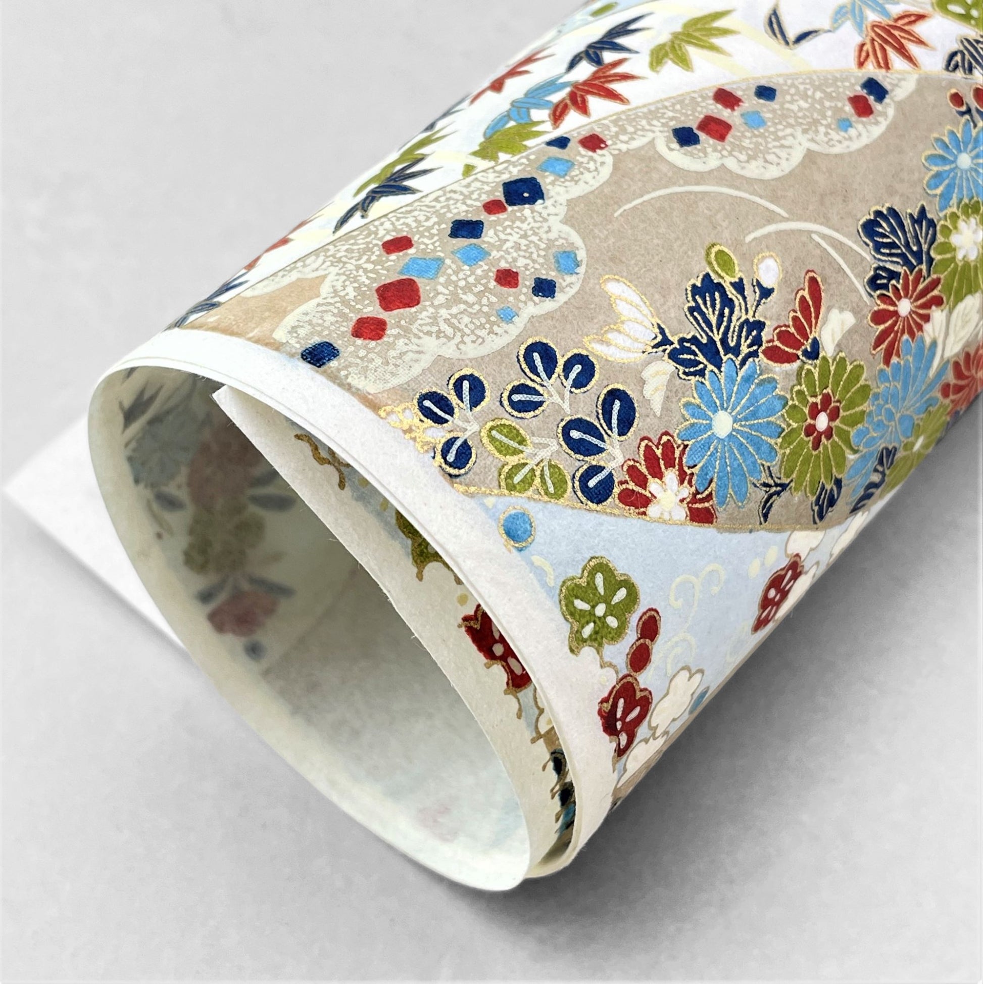 japanese silk-screen handmade paper showing taupe and pale blue waves pattern with multicolour flowers and foliage, with gold accents