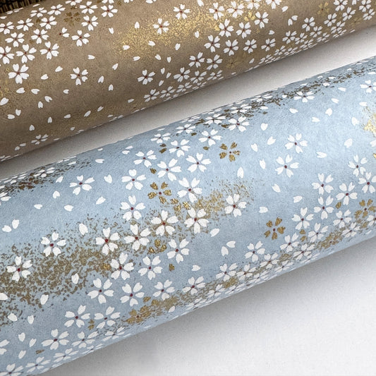 a sheet of Japanese silkscreen printed chiyogami paper with waves of tiny white and gold flowers on a soft aqua background with a dusting of gold. close up