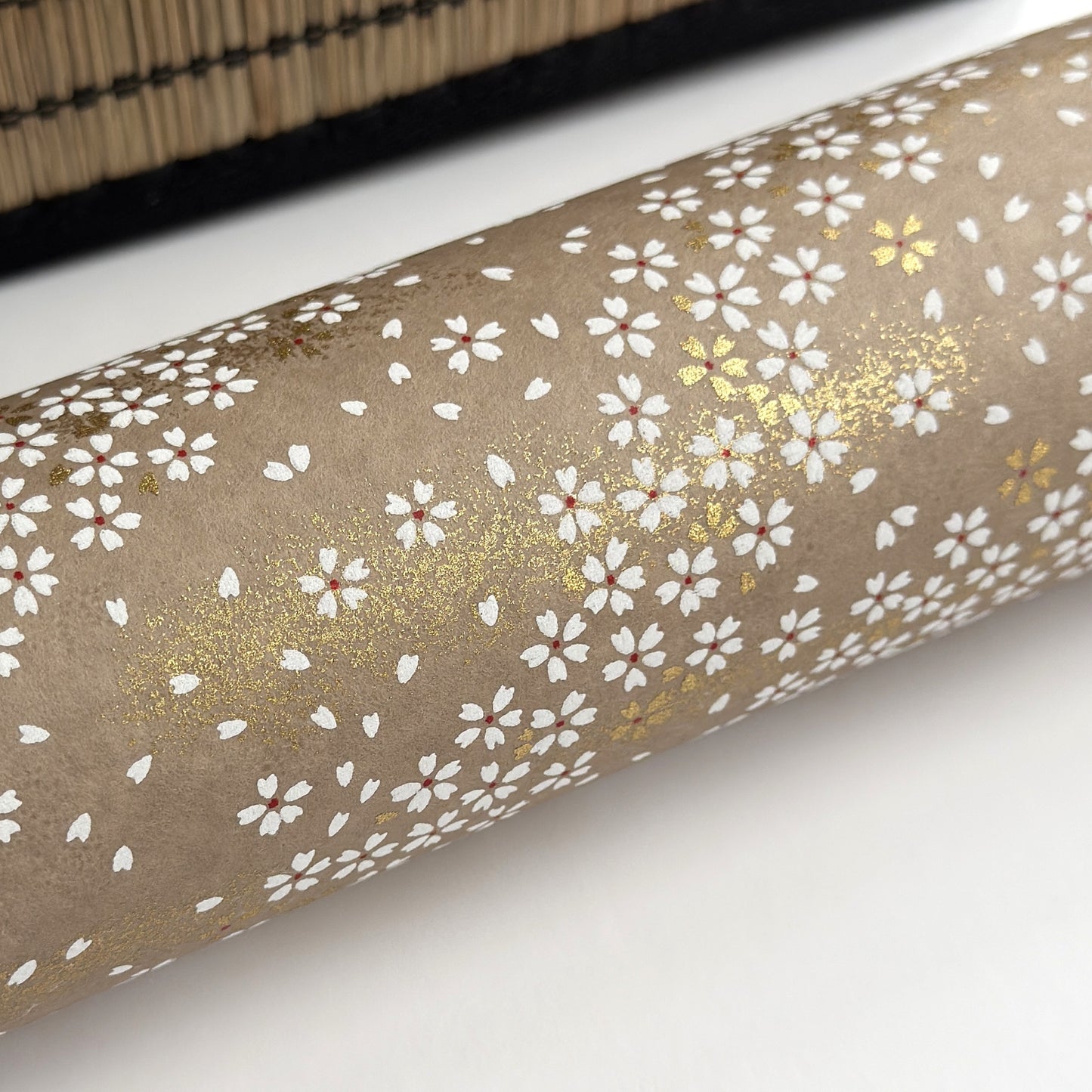 a sheet of Japanese silkscreen printed chiyogami paper with waves of tiny white and gold flowers on a soft taupe background with a dusting of gold. close up