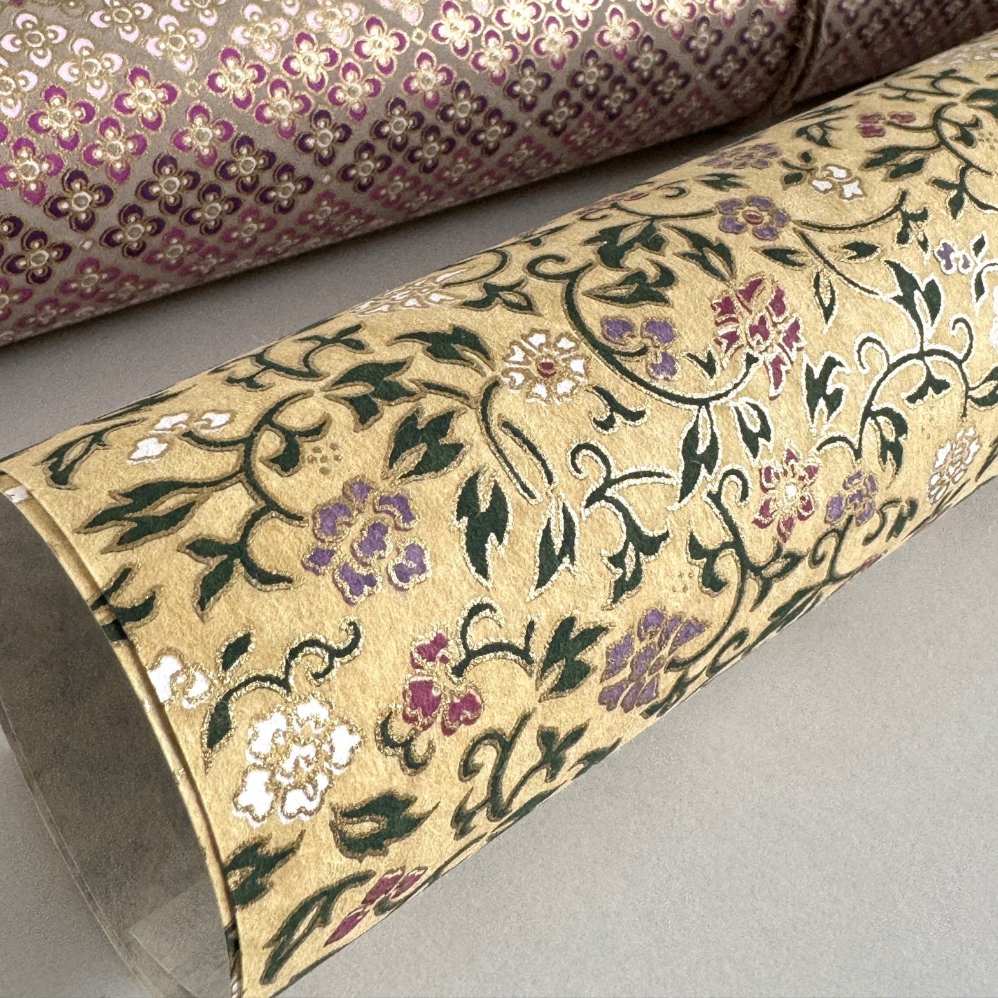 Japanese chiyogami silkscreen paper with a dainty floral pattern on a creamy backdrop and finished with gold metallic ink. Pictured rolled