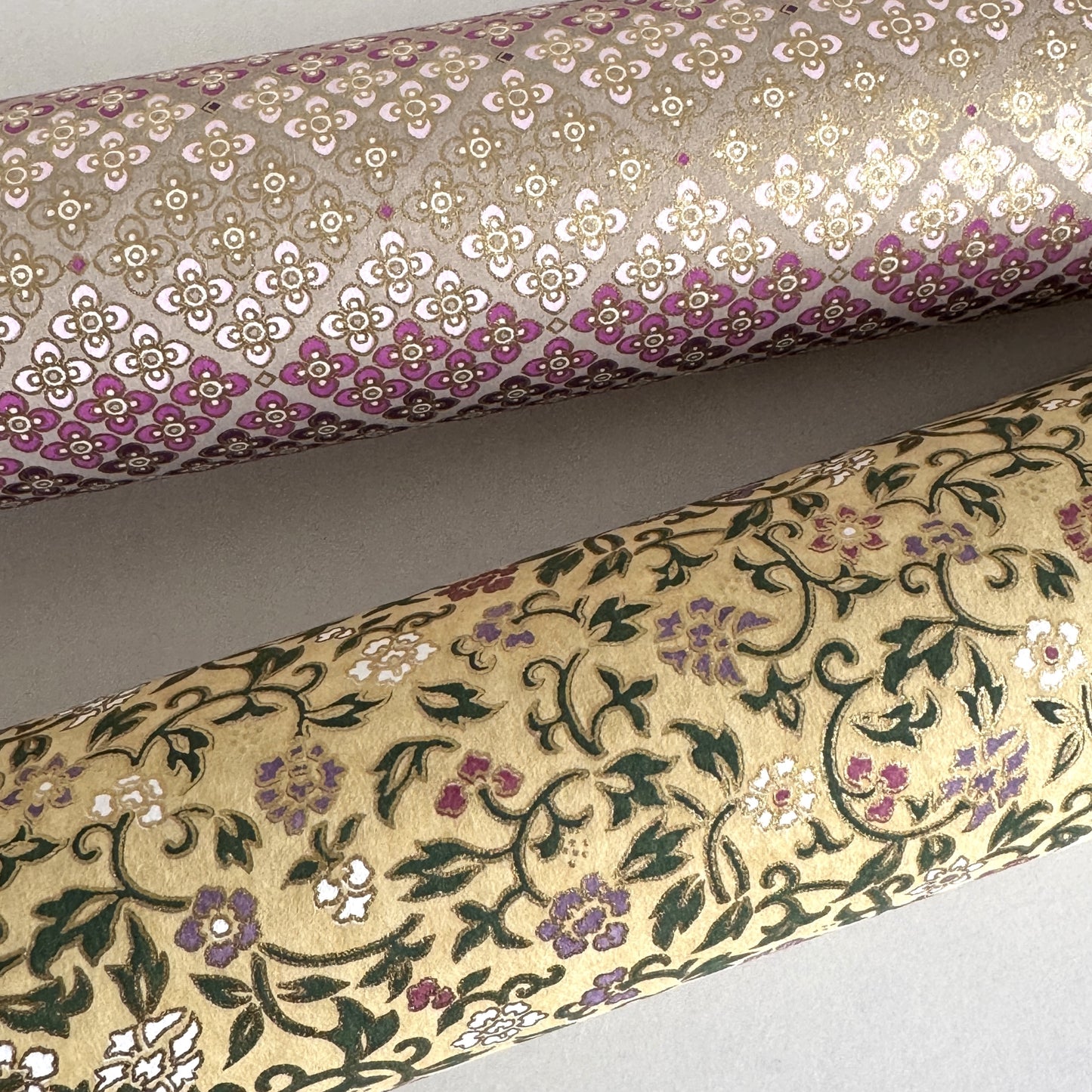 Japanese chiyogami silkscreen paper with a dainty floral pattern on a creamy backdrop and finished with gold metallic ink. pictured rolled alongside another paper