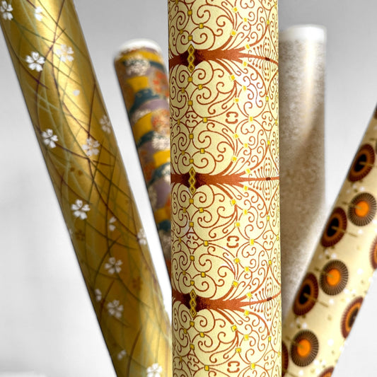 Japanese silkscreen chiyogami paper with a intricate filigree trellis design in brown with gold accent, close up of sheet rolled
