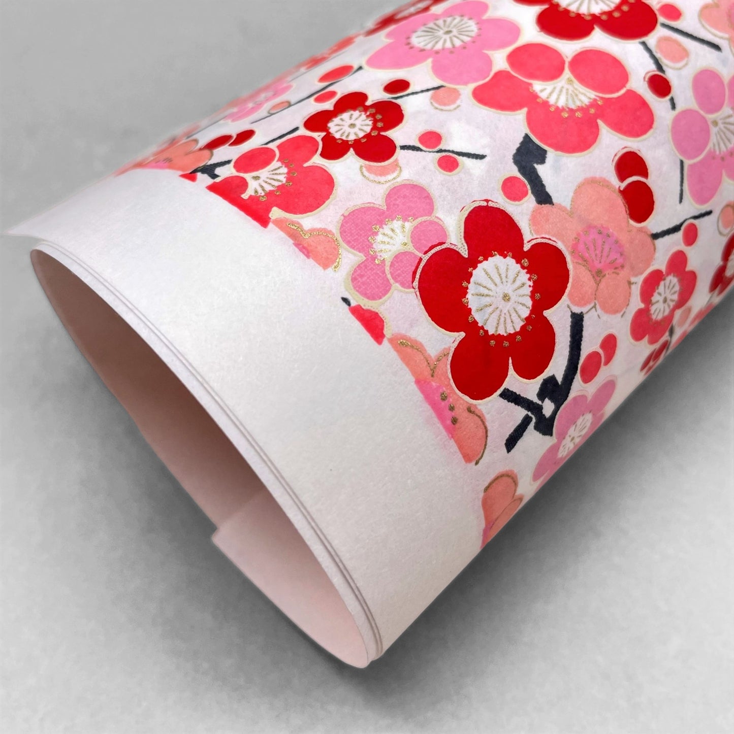 japanese silk-screen handmade paper showing pink and red plum flower repeat pattern with gold highlights