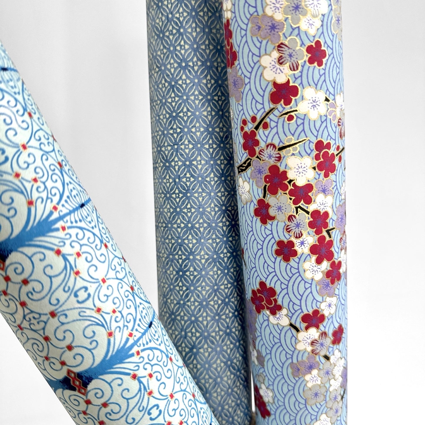Japanese silkscreen chiyogami paper with a two-tone sky blue geometric pattern on creamy white. Pictured rolled with other designs
