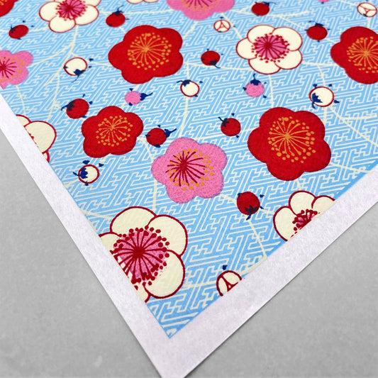 japanese silk-screen handmade paper showing red and pink plum flowers on a blue geometric backdrop