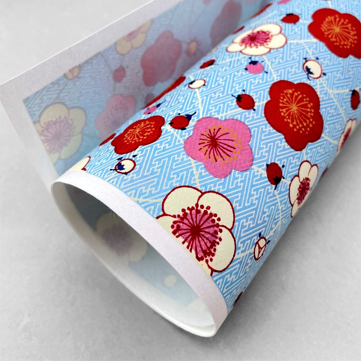 japanese silk-screen handmade paper showing red and pink plum flowers on a blue geometric backdrop