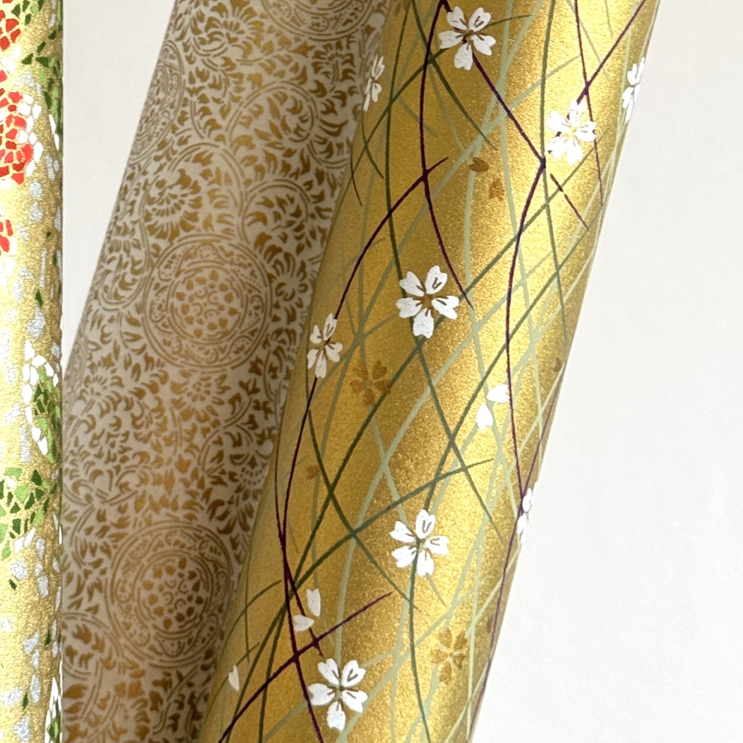 Japanese silkscreen chiyogami paper with a pattern of purple arches and white cherry blossom on antique gold backdrop. Close up