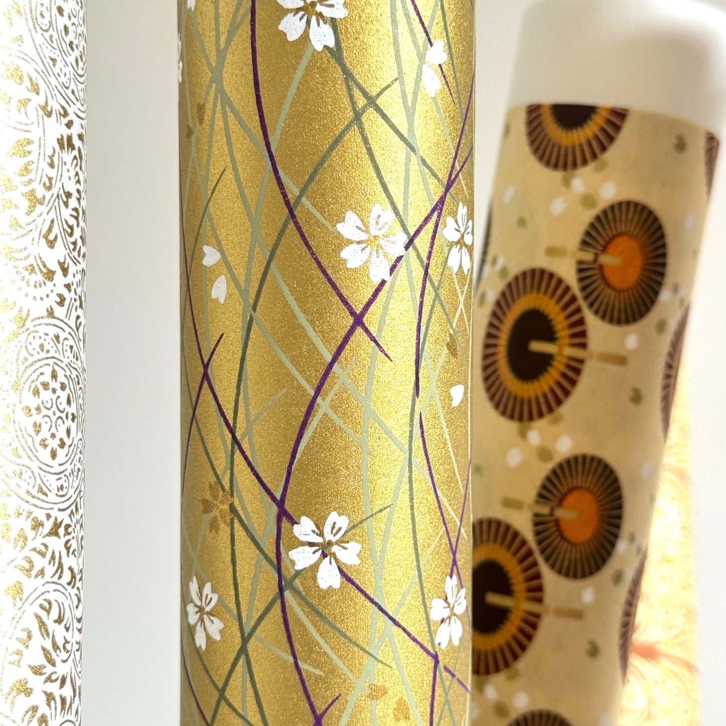 Japanese silkscreen chiyogami paper with a pattern of purple arches and white cherry blossom on antique gold backdrop. Close up rolled
