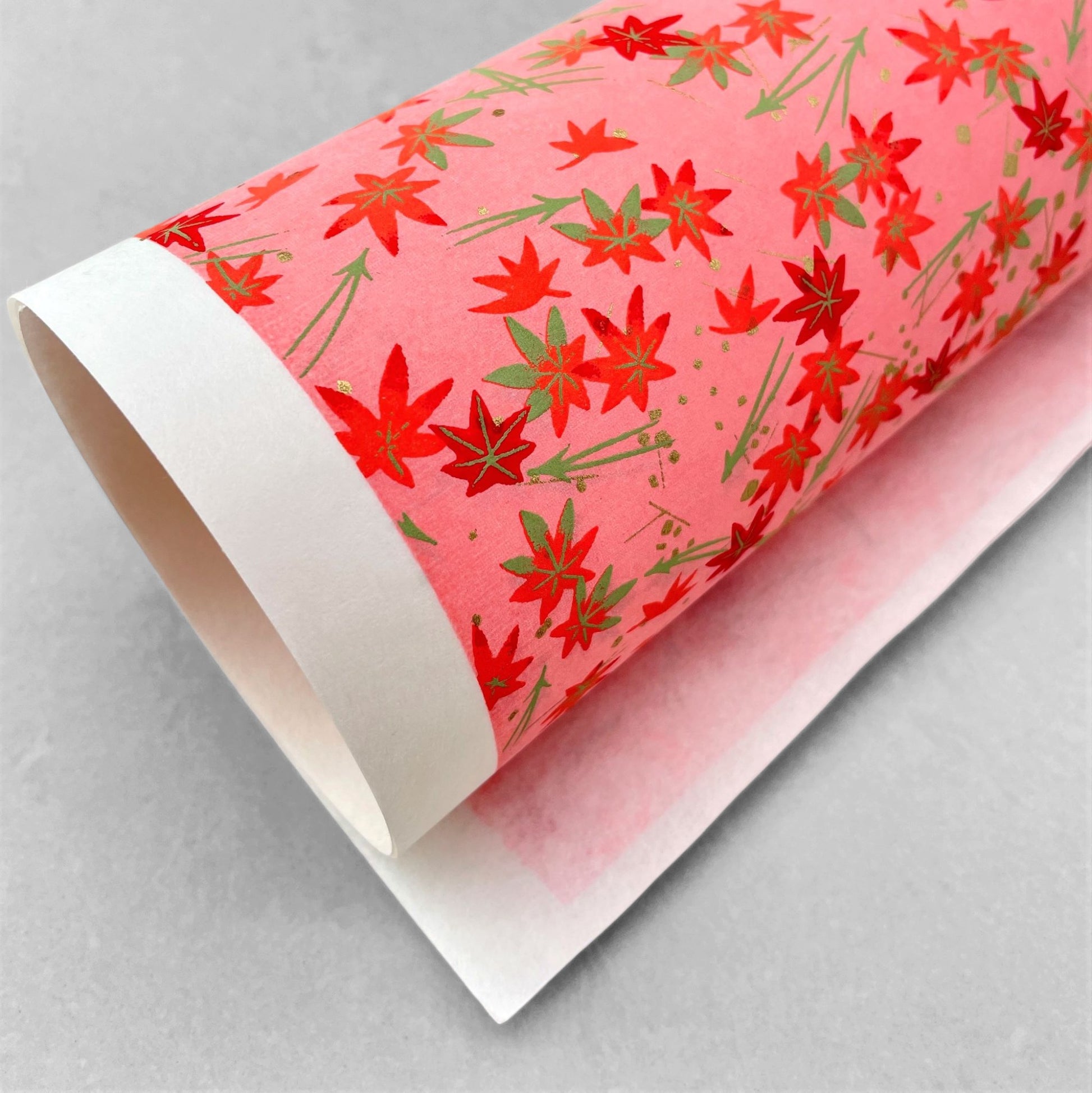 japanese silk-screen handmade paper showing pattern of red falling leaves on coral backdrop and gold highlights