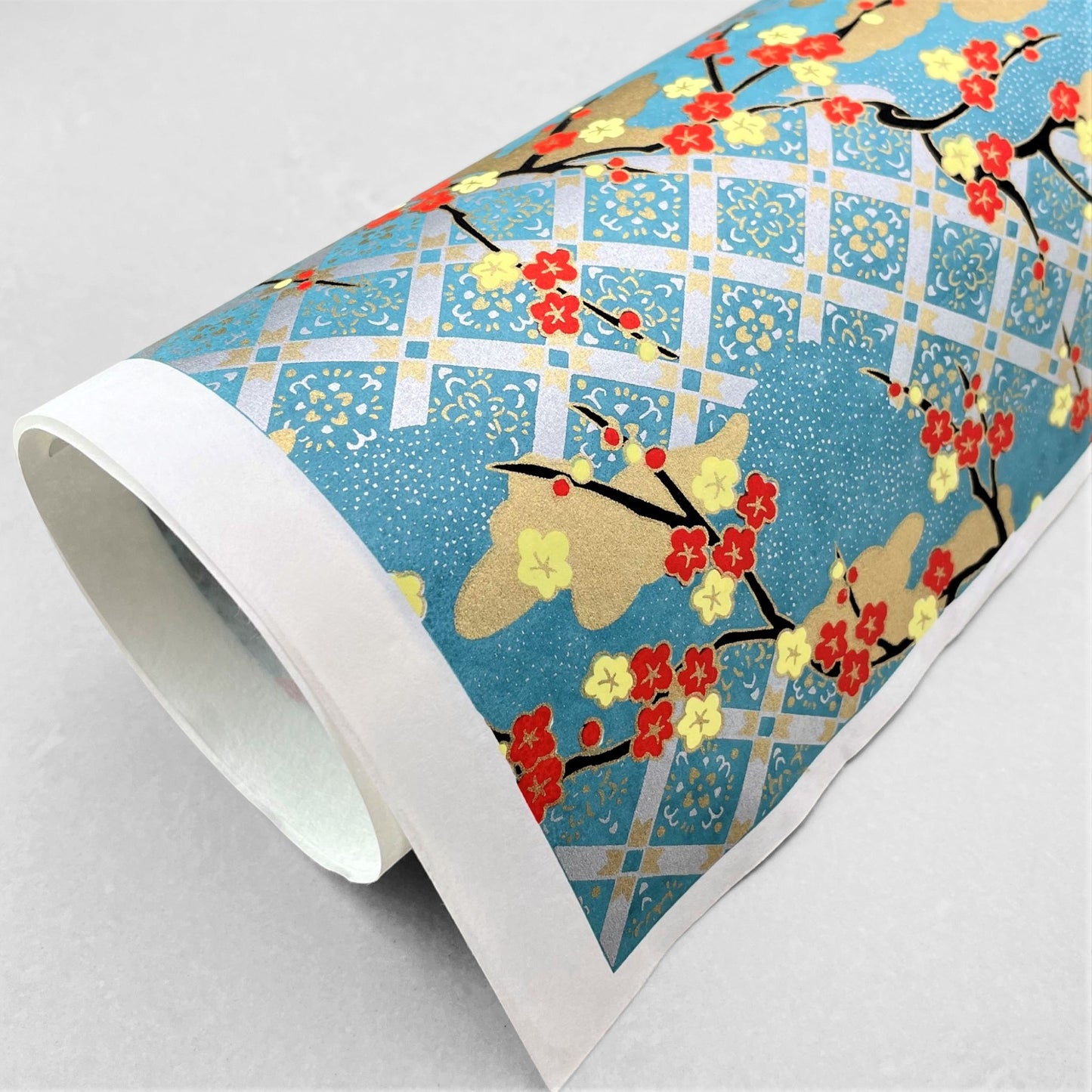 japanese silk-screen handmade paper showing branches of red blossom, gold clouds on a teal, gold and silver geometric backdrop.