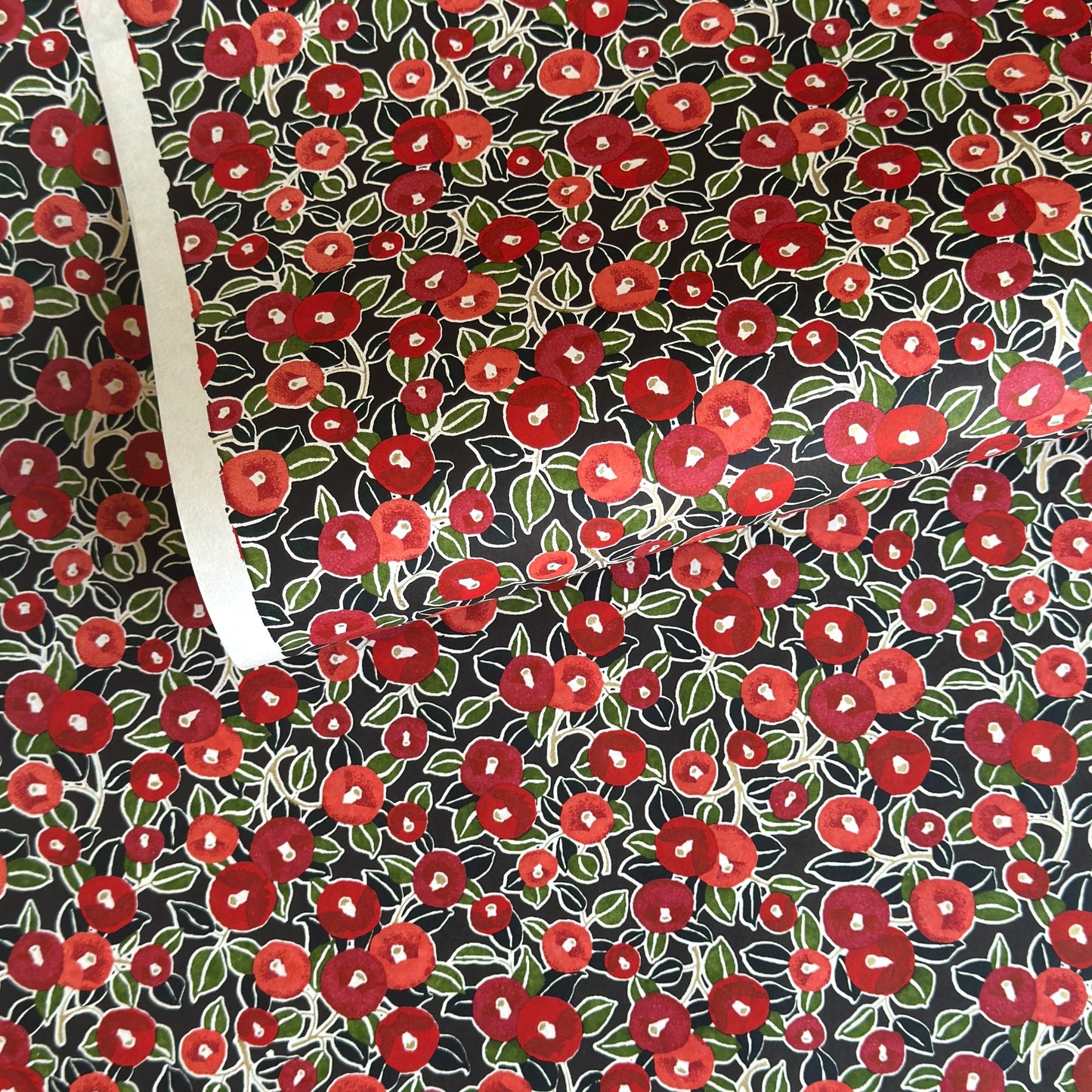 japanese silk-screen handmade paper, chiyogami, with a design showing red and pink camellia flowers and green leaves on black background