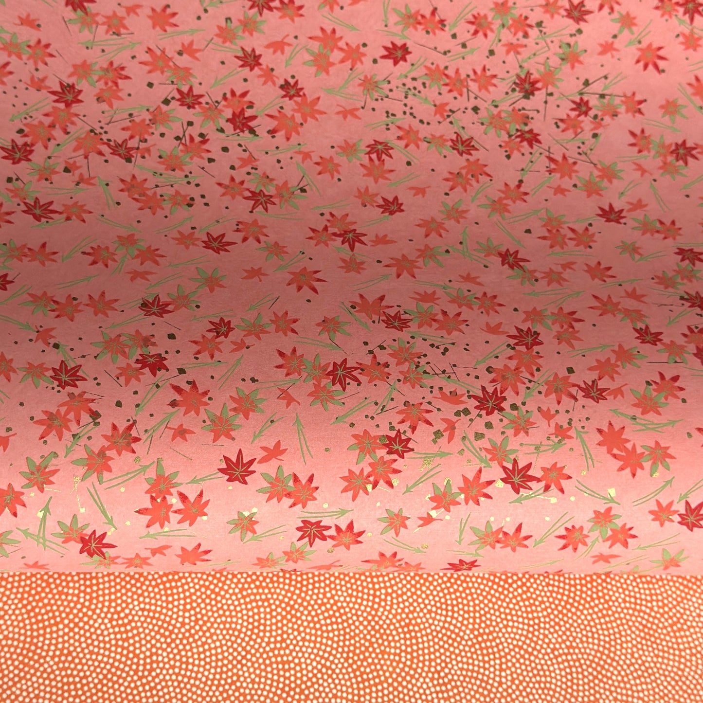 japanese silk-screen handmade paper showing pattern of red falling leaves on coral backdrop and gold highlights