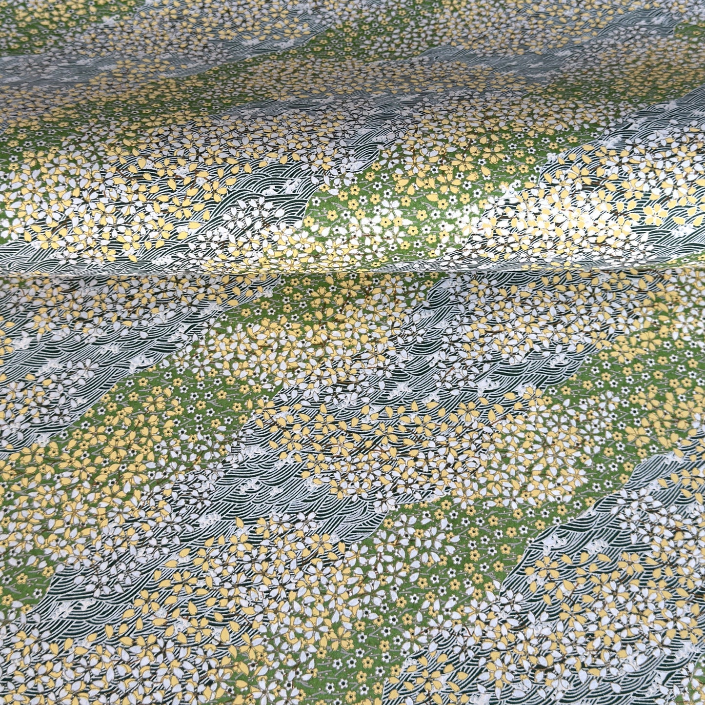 Japanese silkscreen chiyogami paper with a pattern of dark green rivers and grass green banks with an abundance of little flowers in white and yellow